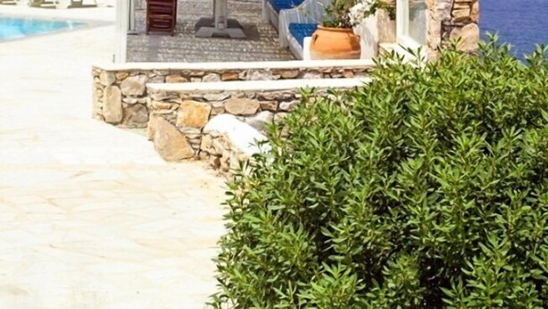 Un área de estar al aire libre de piedra con piscina y sillones de descanso, con vistas al mar.