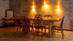 Un comedor rústico con una mesa y sillas de madera, una pizarra a la izquierda y tres lámparas colgantes.
