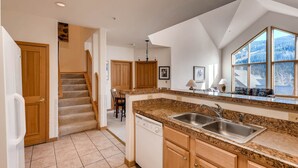 A kitchen with granite countertops, a dishwasher, and a large window with a view of trees. - Gateway 5039 (Keystone)