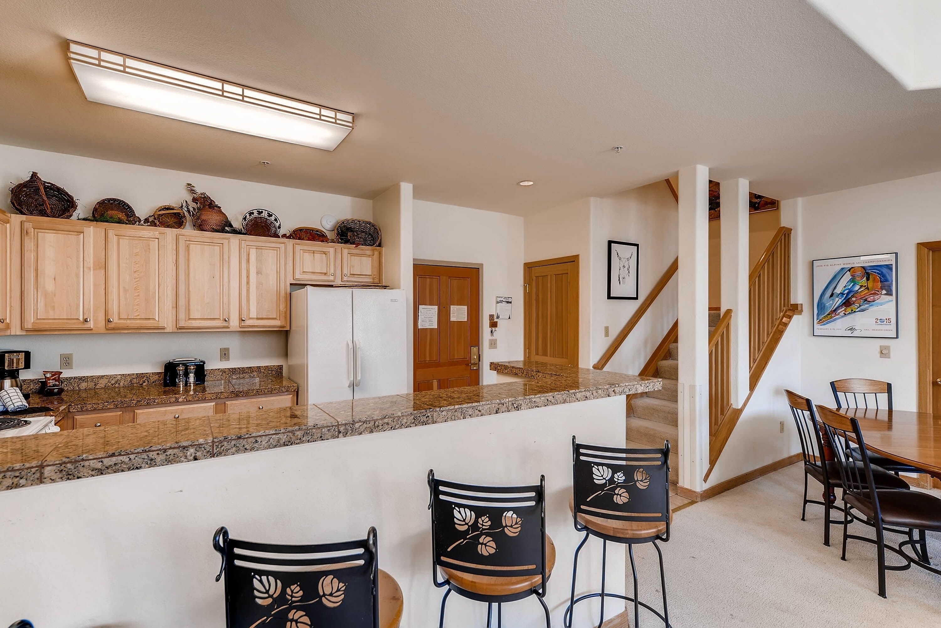 A kitchen with wooden cabinets, a granite countertop, and a bar area with stools.