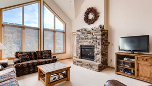 A living room with a stone fireplace, a large window, a sofa, a coffee table, and a television on a wooden stand. - Gateway 5039 (Keystone)