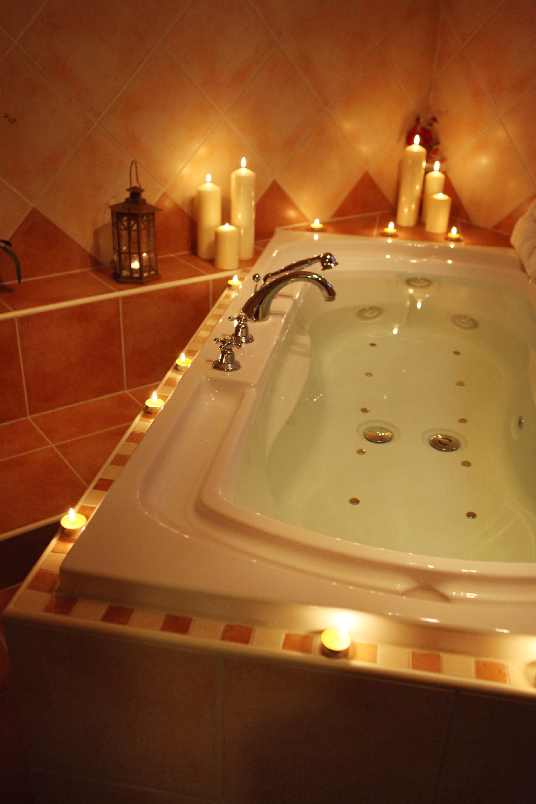 A bathtub with multiple candles and a lantern, surrounded by tiled walls.