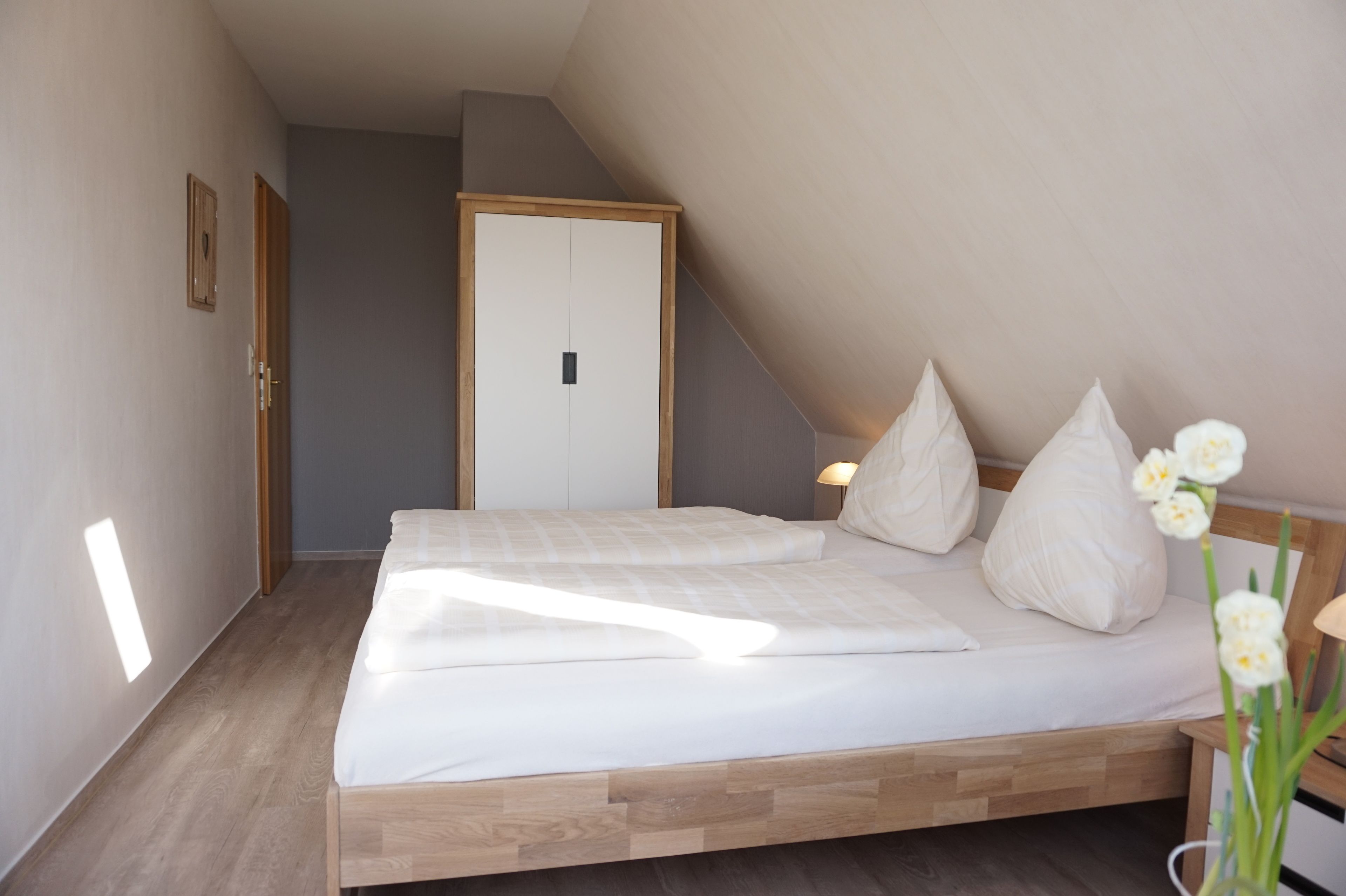 Quarto com estrutura de cama de madeira, roupa de cama branca e uma pequena mesa de cabeceira com abajur.