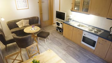 Un espacio habitable compacto con un sofá, una mesita redonda, un televisor, una cafetera y una kitchenette con estufa y lavamanos.