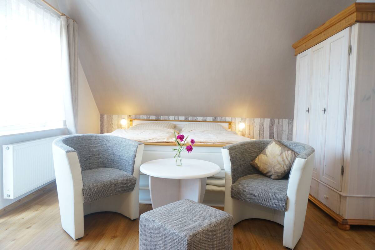 A bedroom with a bed, two armchairs, a small round table, and a cabinet.
