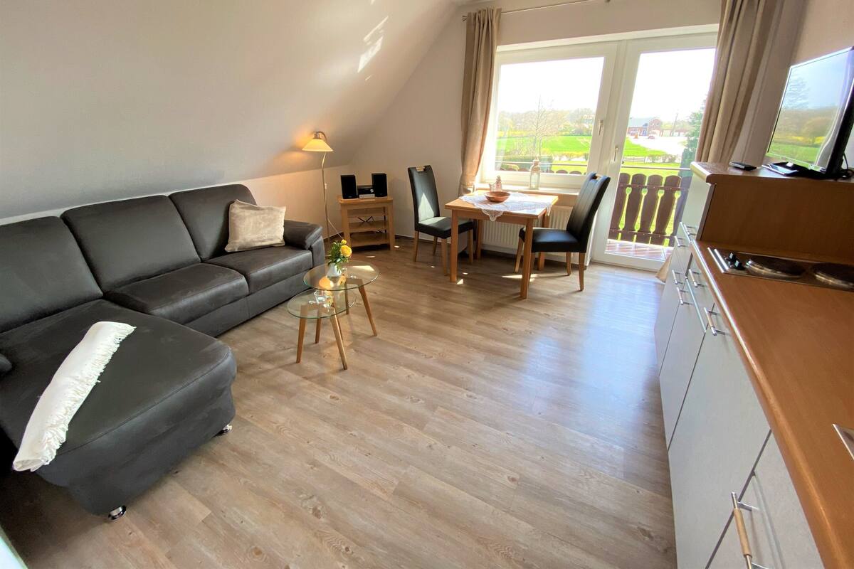 A modern living room with a black sofa, a glass coffee table, and a dining area with a table and chairs.