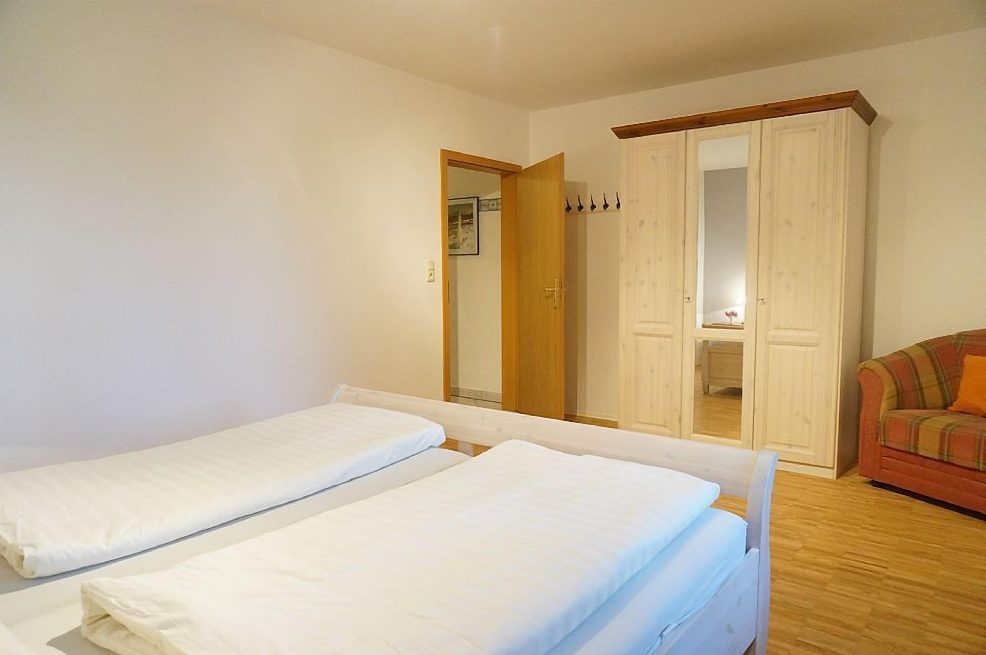 A room with two single beds, a wooden floor, a wardrobe, and a sofa.