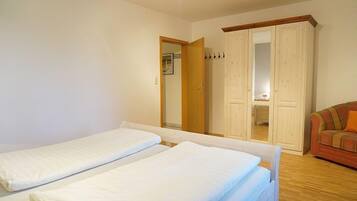 A room with two single beds, a wooden floor, a wardrobe, and a sofa.