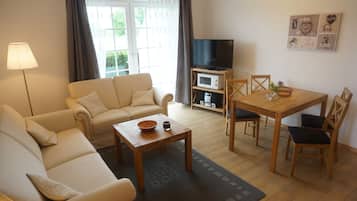 Un salon comprenant un canapé, une table basse, un téléviseur et un coin repas avec des chaises et une table.