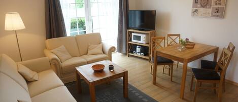 A living room with a sofa, coffee table, TV, and dining area with chairs and a table.