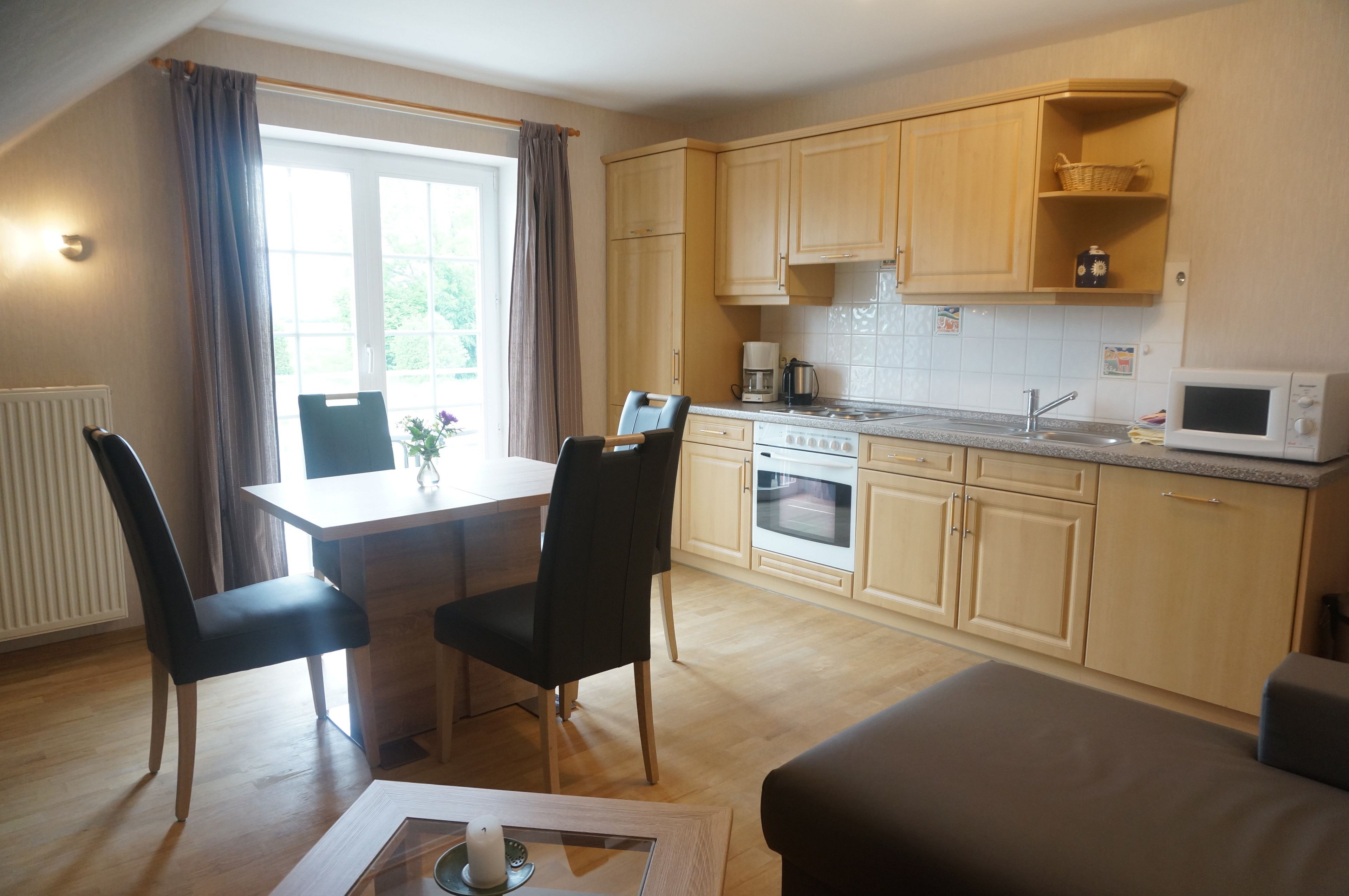 A compact kitchen with wooden cabinets, a dining table with chairs, a microwave, and a coffee maker.