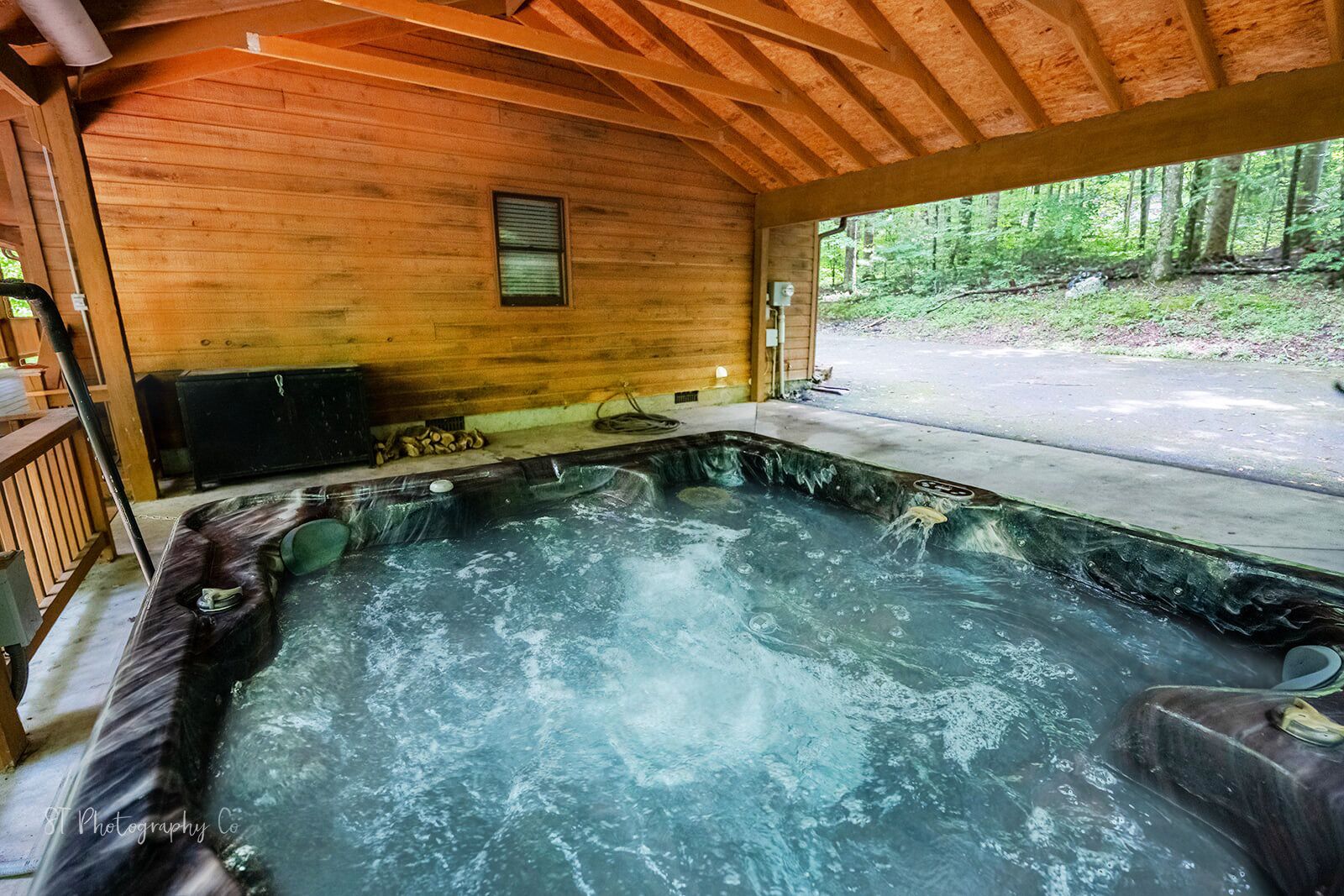A hot tub in a wooden cabin with a view of a forest.