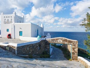 A white building with blue doors and windows, a stone pathway, and a view of the sea. - Cavo Delos (Mykonos)