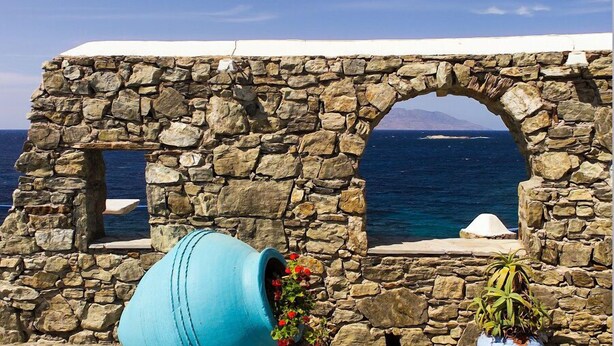 A stone wall with a view of the sea, a large blue pot, and a potted plant. - Cavo Delos (Mykonos)