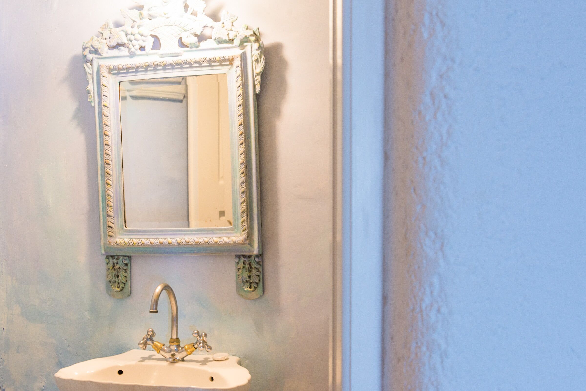 A bathroom with a white sink and an ornate mirror with a decorative frame.