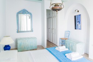 A bedroom with a bed, a dresser, a chair, a lamp, and a door. - Cavo Delos (Mykonos)