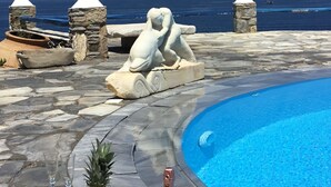 A pool area with a statue, a bottle of champagne, and fruit. - Cavo Delos (Mykonos)