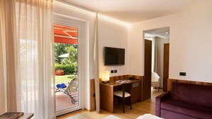 Quarto de hotel com cama, escrivaninha, cadeira, televisão e sofá.