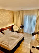 Habitación de hotel con una cama grande, un escritorio, una silla, una mesita y una ventana con cortinas.