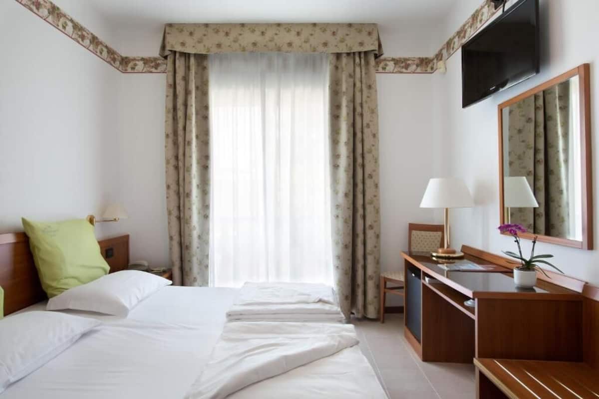 A hotel room with a bed, a desk, a chair, a TV, and a window with curtains.