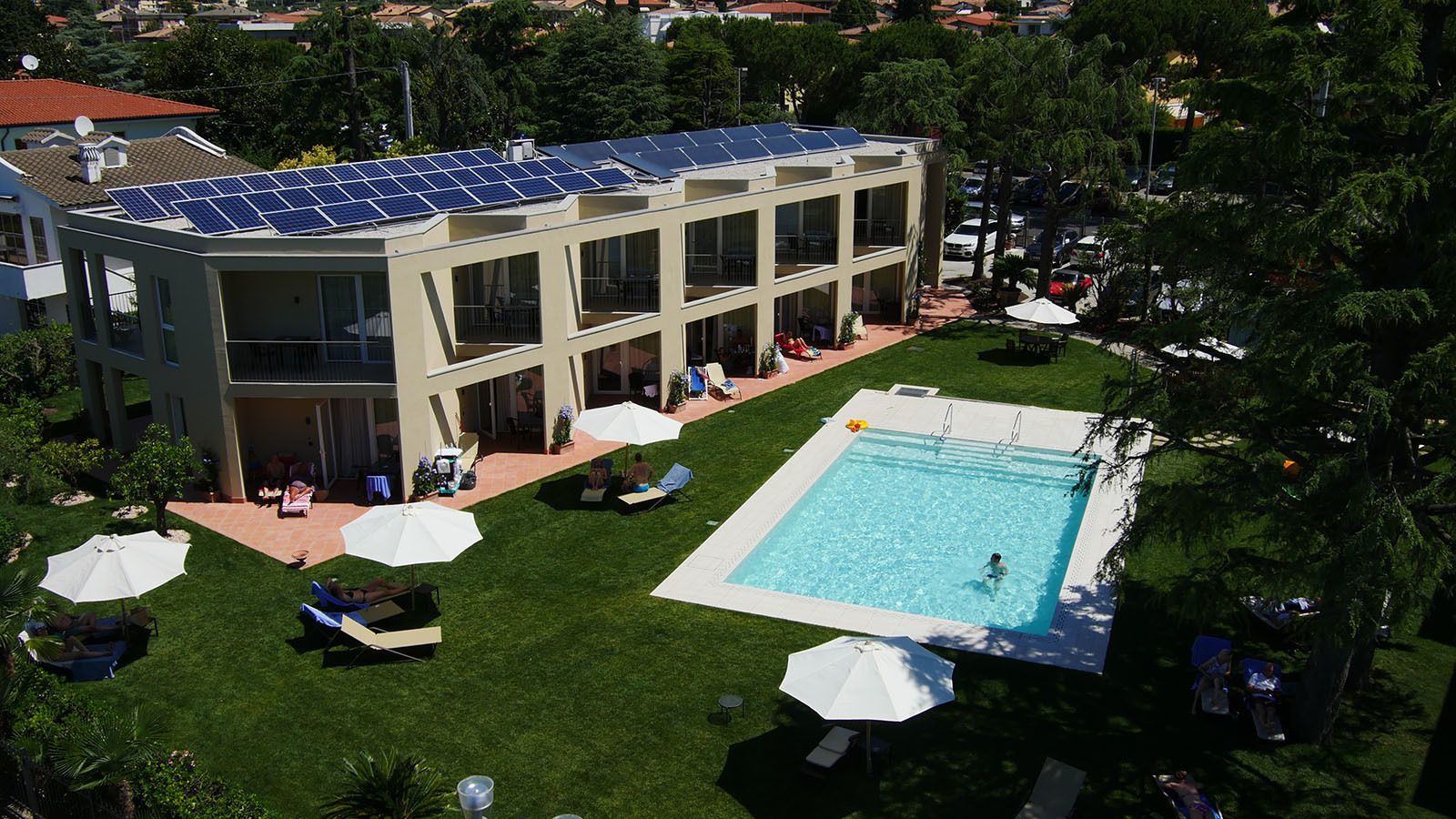 Un edificio moderno con una instalación de paneles solares en la azotea, una piscina y zonas de estar al aire libre.