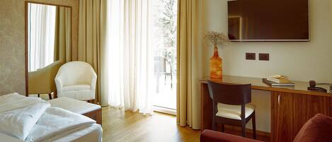 A hotel room with a bed, two chairs, a desk, a TV, and a window with curtains.