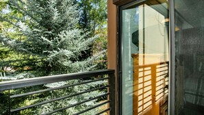Ein Balkon mit Metallgeländer, der auf einen Garten mit Nadelbäumen blickt.