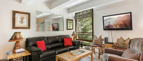 A living room with a black leather sofa, a wooden coffee table, and a television on the wall.