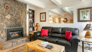 Ein Wohnzimmer mit Kamin aus Stein, einer schwarzen Ledersofa mit roten Kissen, einem Couchtisch aus Holz und einem Bücherregal.