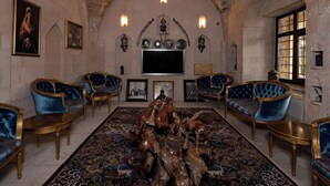 Uma sala imponente com um tapete grande e ricamente decorado, várias poltronas estofadas em azul e uma escultura de madeira como peça central.