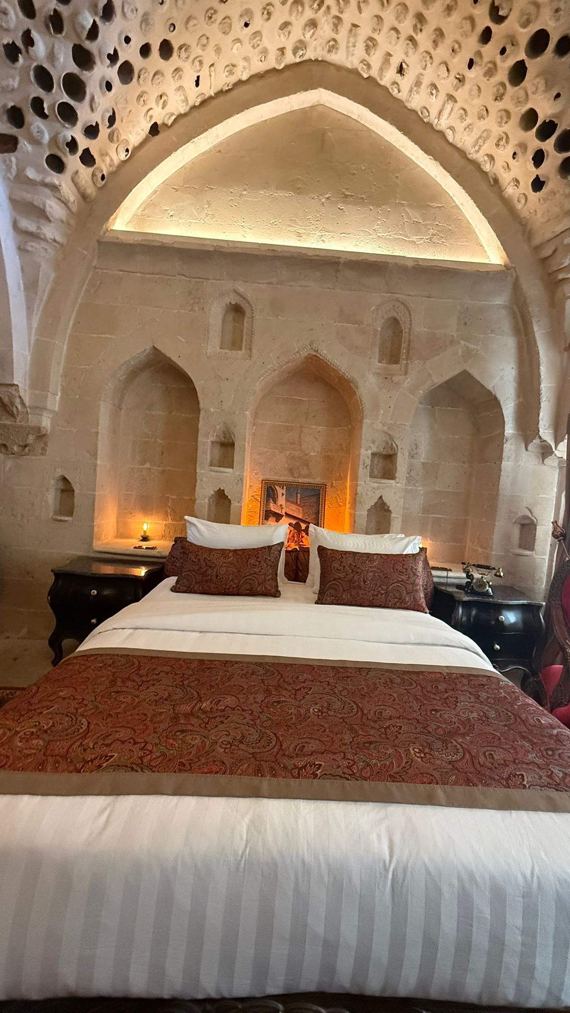 A bedroom with a large bed, a fireplace, and arched stone walls.