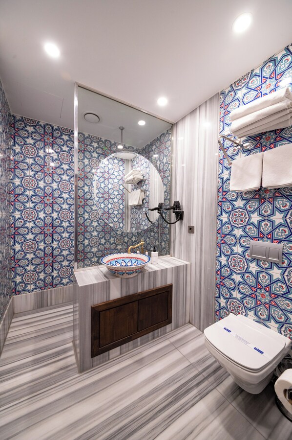 Un baño con suelo de mármol, un lavabo con una pila decorativa, un inodoro y una zona de ducha con puerta de cristal.