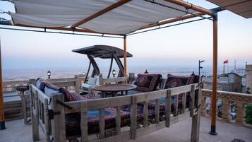 An outdoor seating area with a view of the cityscape, featuring a wooden pergola, cushioned seating, and a small table.