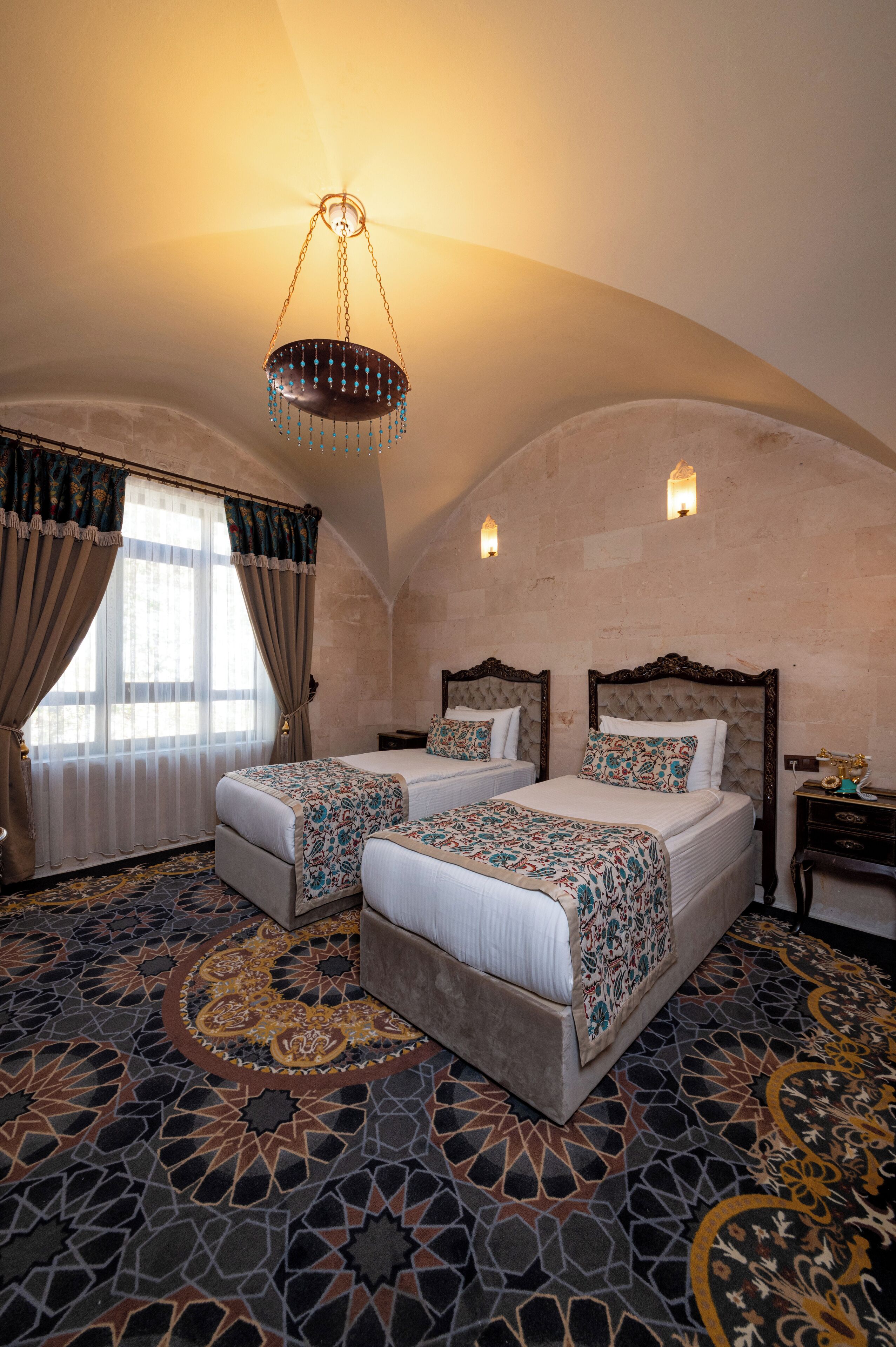 A room with two beds, a chandelier, and a patterned carpet.