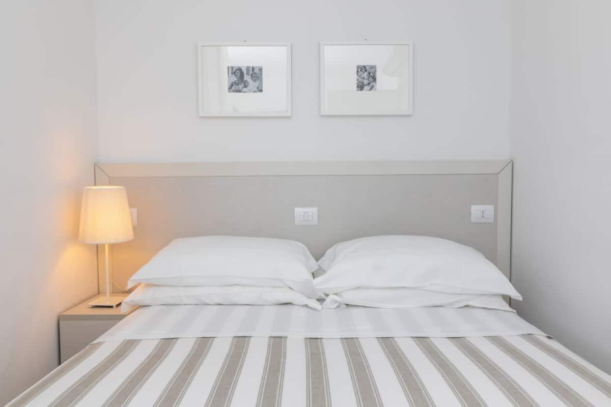 A neatly made bed with striped bedding, a bedside lamp, and two framed pictures on the wall.