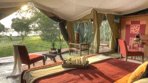 Una habitación con carpa, una cama, una mesa con una bandeja de objetos, una silla y vistas al exterior.