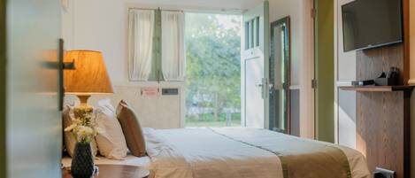 Habitación de hotel con cama, mesita de noche con lámpara, televisor montado en la pared y ventana con cortinas.