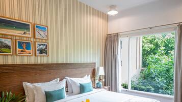 Una habitación de hotel con una cama grande, un ventilador de techo, una ventana con cortinas y cuadros en la pared.