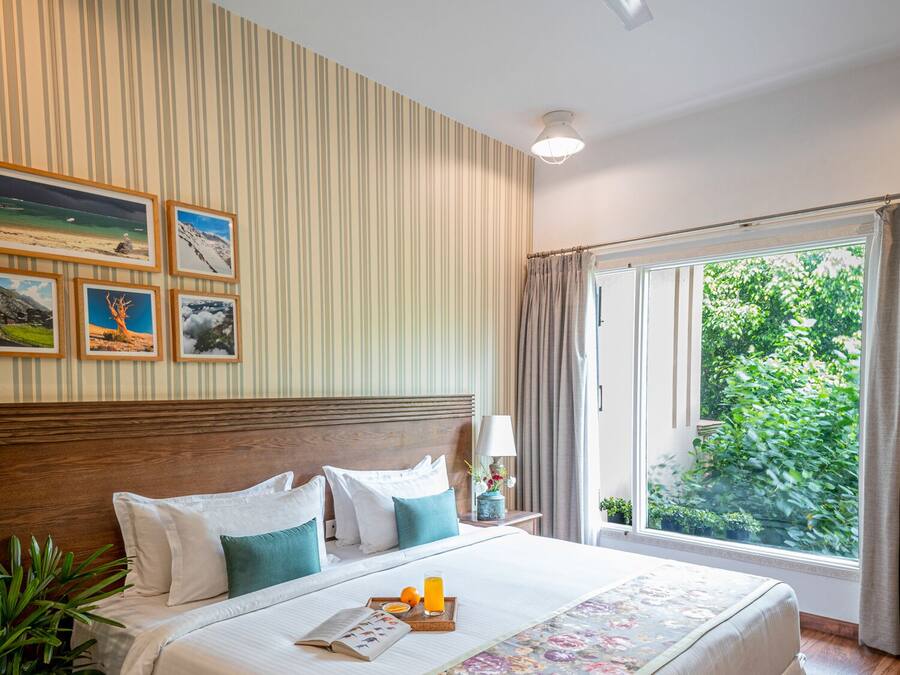 Una habitación de hotel con una cama grande, un ventilador de techo, una ventana con cortinas y cuadros en la pared.