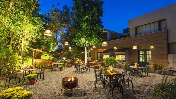 An outdoor patio area with tables and chairs, surrounded by plants and a fire pit. - Karma Chalets (Gurugram)