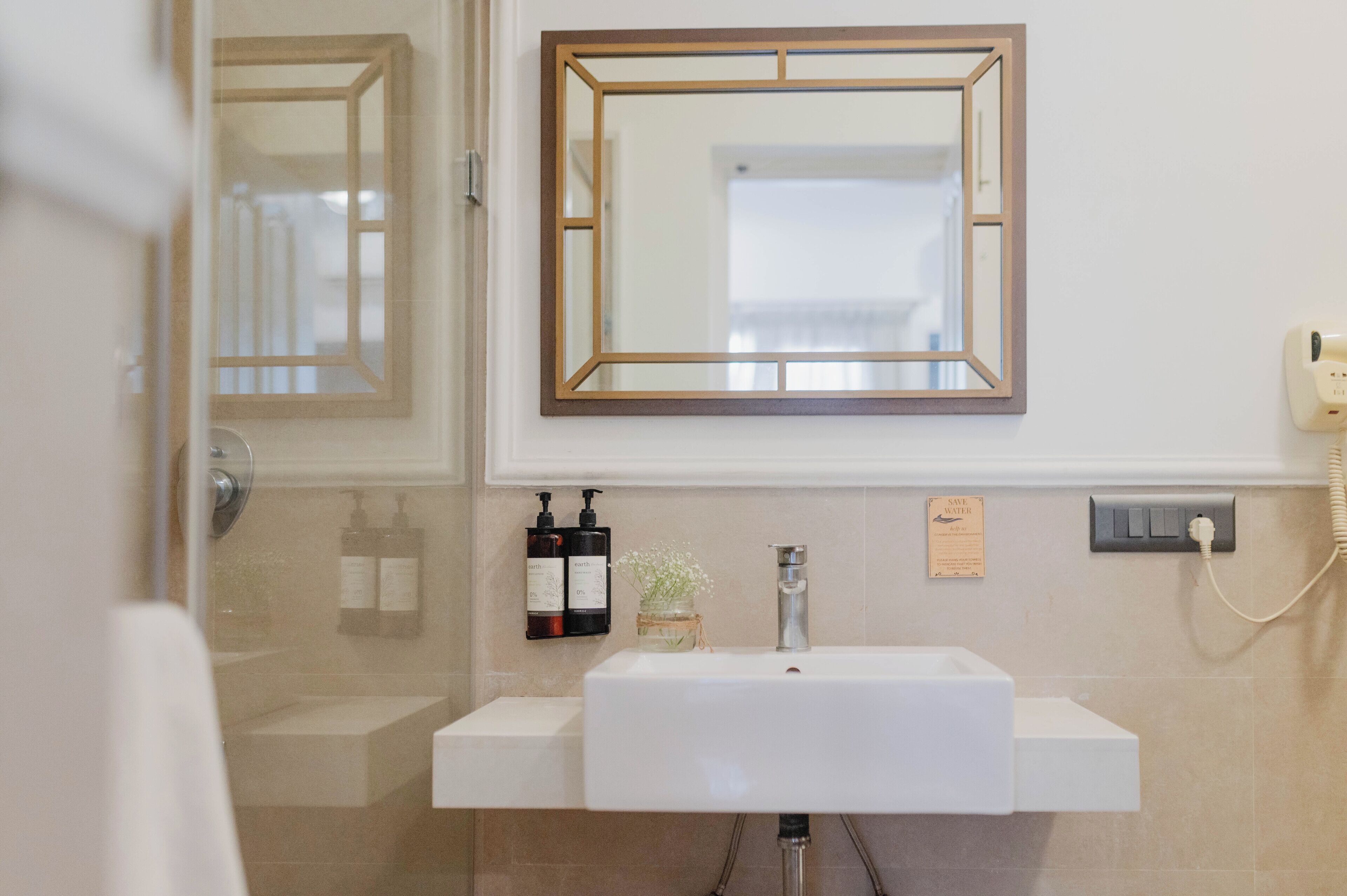 A bathroom with a white sink, a mirror with a wooden frame, two bottles of hand soap, and a small vase with flowers.