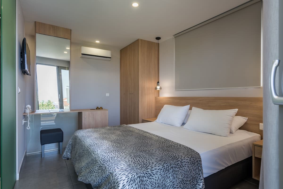 A modern bedroom with a large bed, a bedside table, a mirror, and a window.