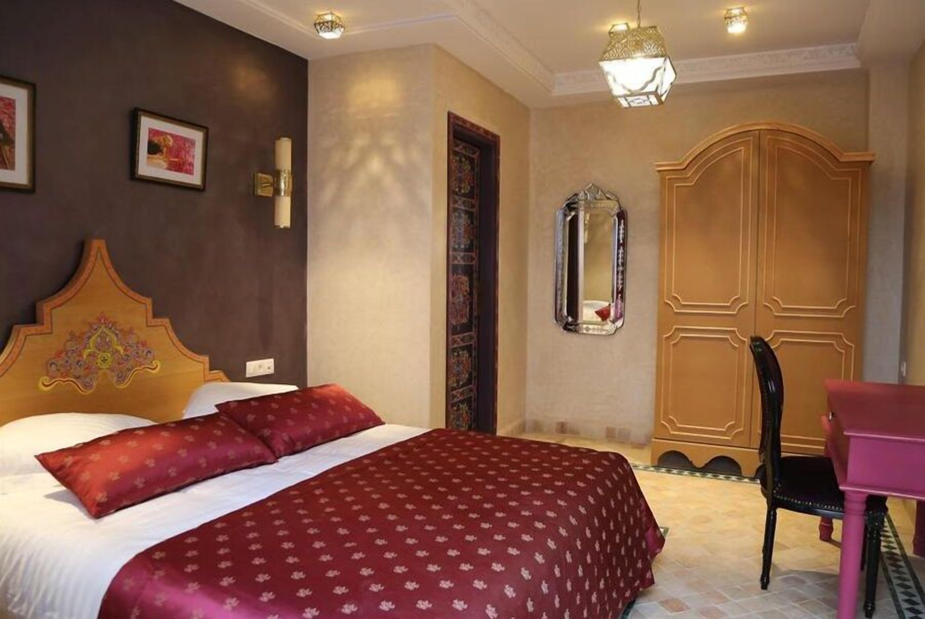 Een hotelkamer met een groot bed, een houten kledingkast, een spiegel en een klein bureau met een stoel.