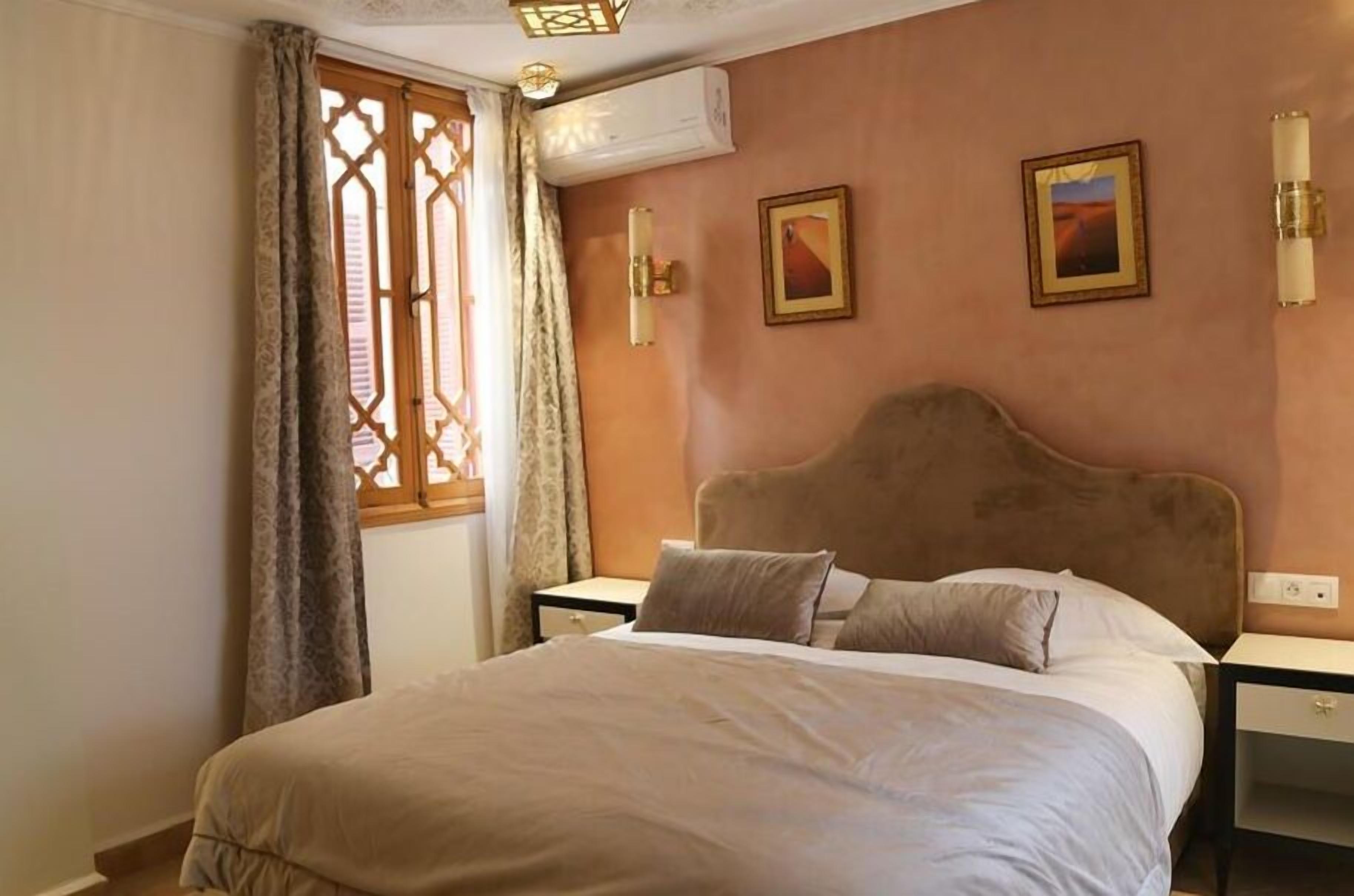 Habitació d'hotel amb un llit gran, una tauleta de nit, un aparell d'aire condicionat i dues làmpades penjades a la paret.