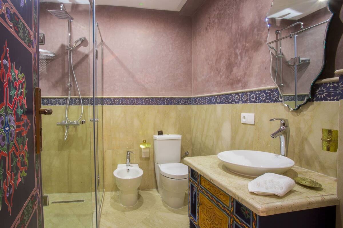 A bathroom with a glass shower enclosure, a sink, a toilet, and a bidet.