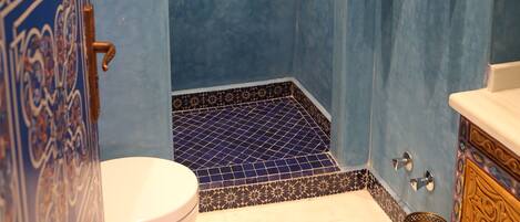 A bathroom with a blue tiled wall, a white toilet, a shower area, and a sink with a gold-colored basin.