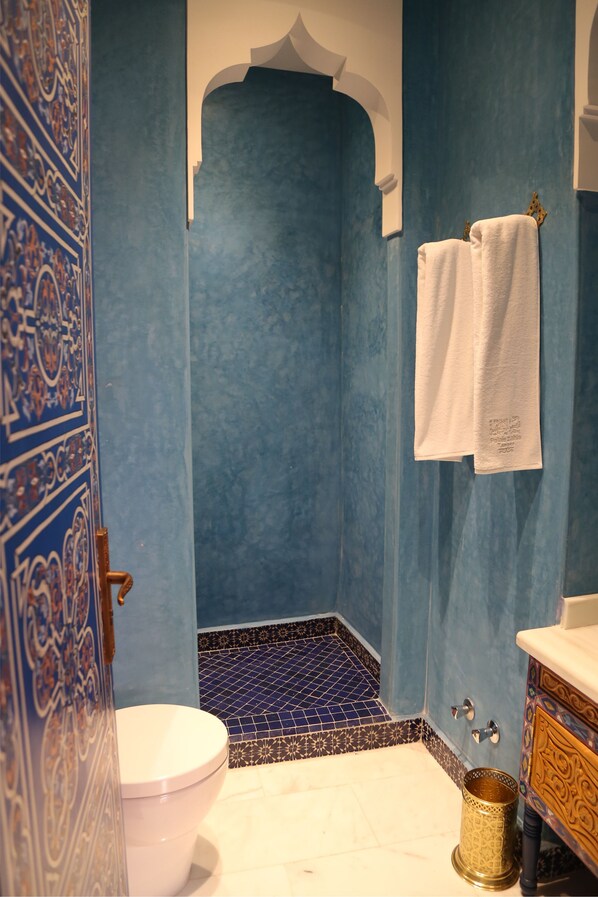 A bathroom with a blue tiled wall, a white toilet, a shower area, and a sink with a gold-colored basin. - Palais Zahia (Tangier)