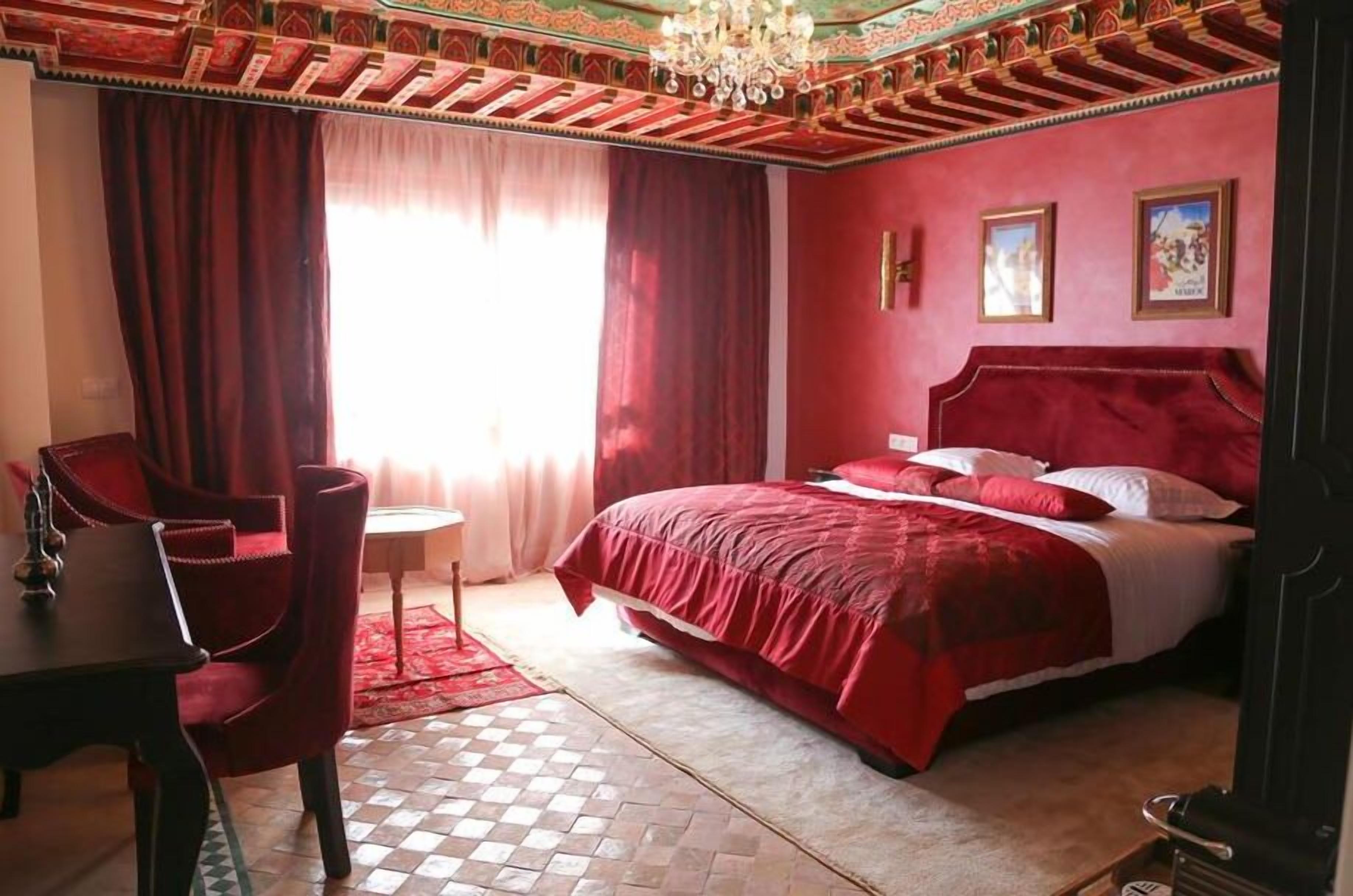 A room with a large bed, red curtains, a chandelier, and a checkered floor.