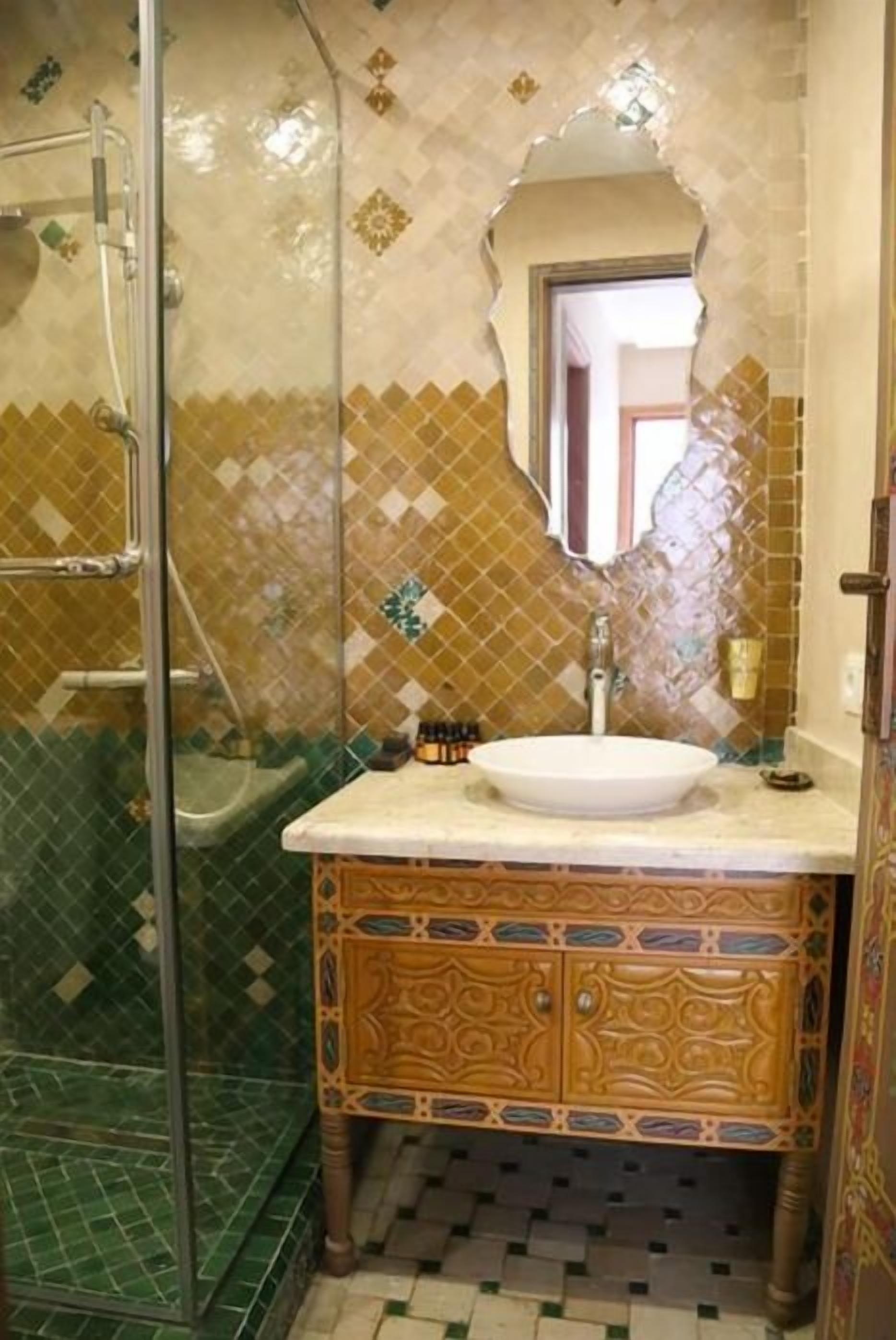 Een badkamer met een douchecabine van glas, een wastafel met een decoratieve kast en betegelde muren.