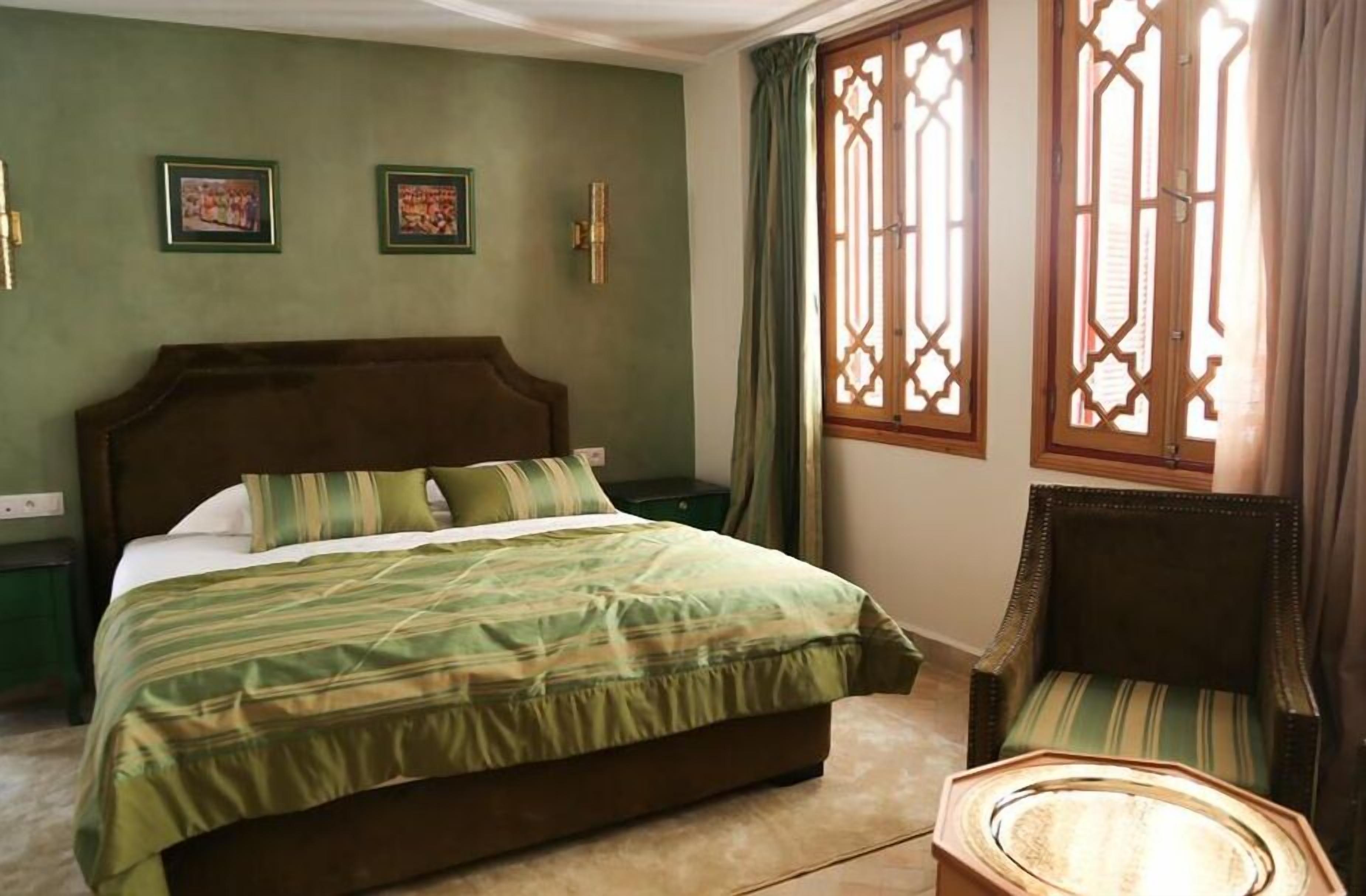 Une chambre avec un grand lit, une chaise et deux fenêtres dotées de cadres en bois décoratifs.
